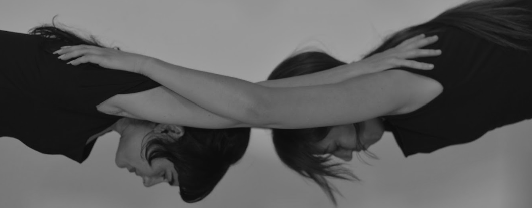Two yoga practitioners supporting one another in a mirrored forward fold
