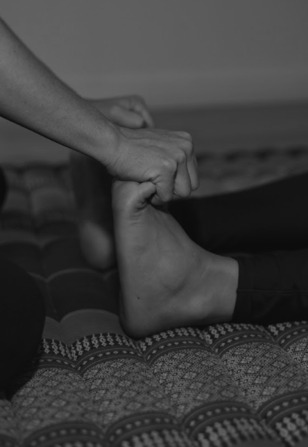 Hands applying focused pressure to a client's foot during Thai yoga massage